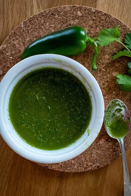 Green sauce in white bowl with fresh jalapeño and cilantro on cork mat and wooden table