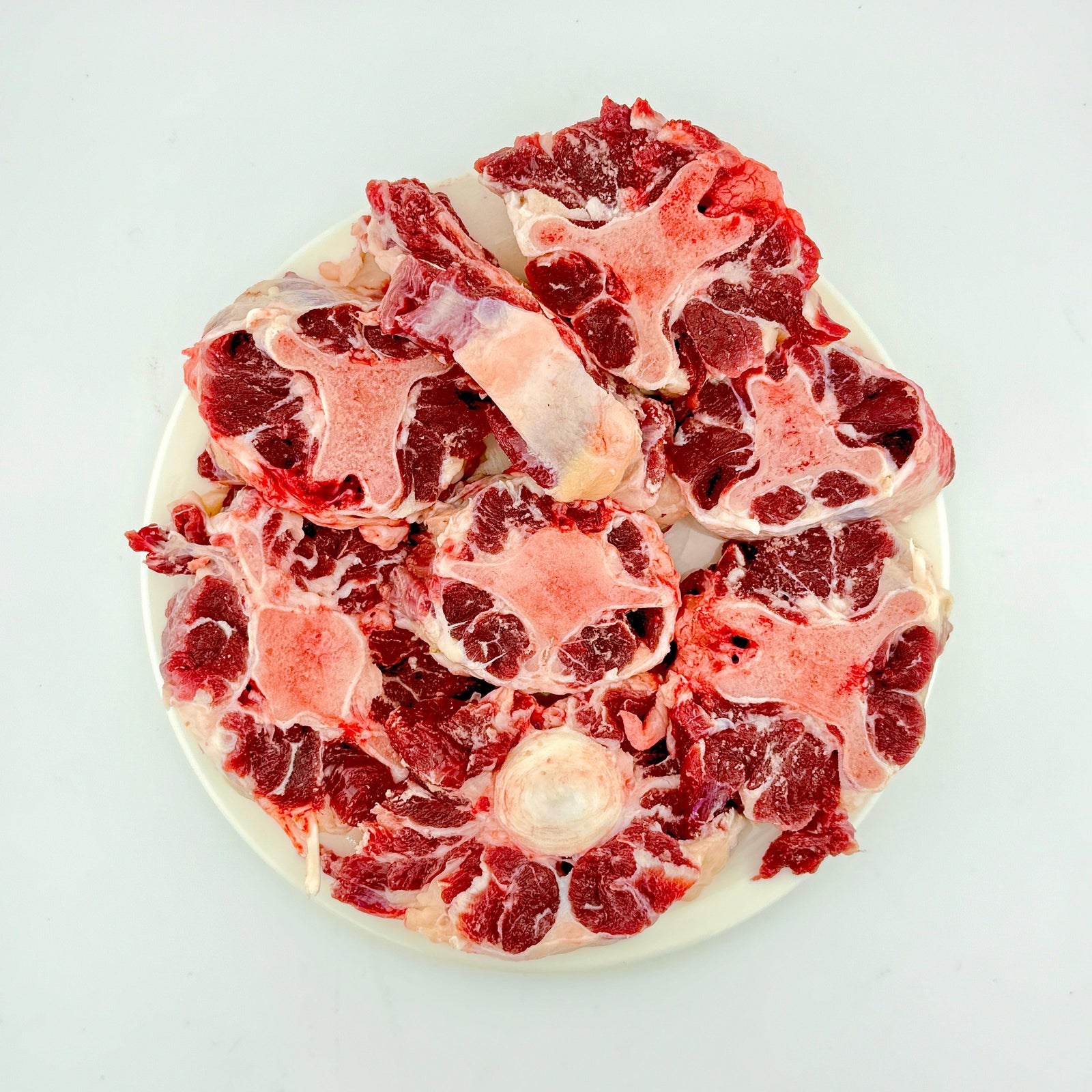 Raw oxtail pieces on a white plate, fresh cut beef for cooking or stews