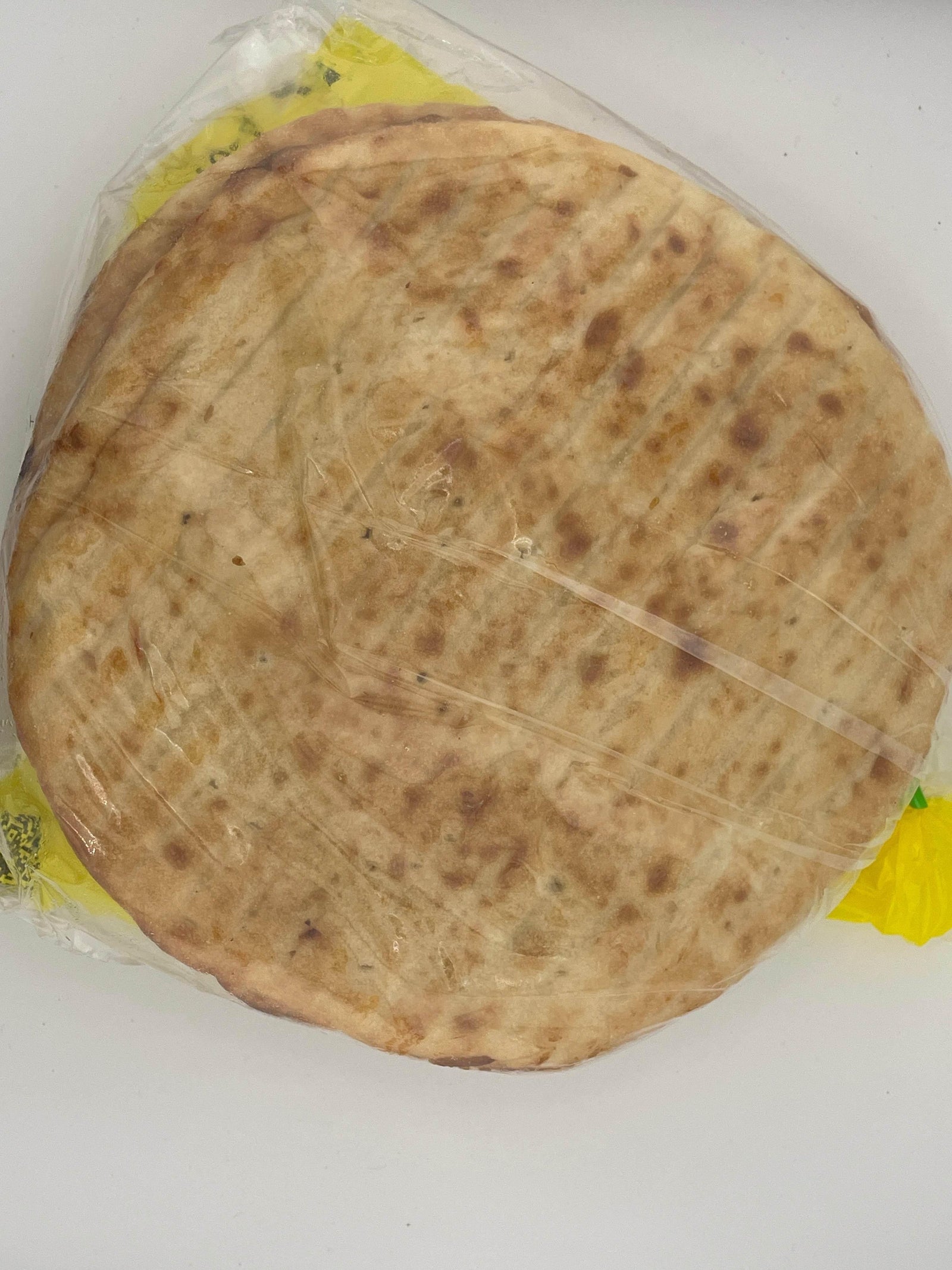 Pack of round grilled flatbread wrapped in clear plastic on white surface