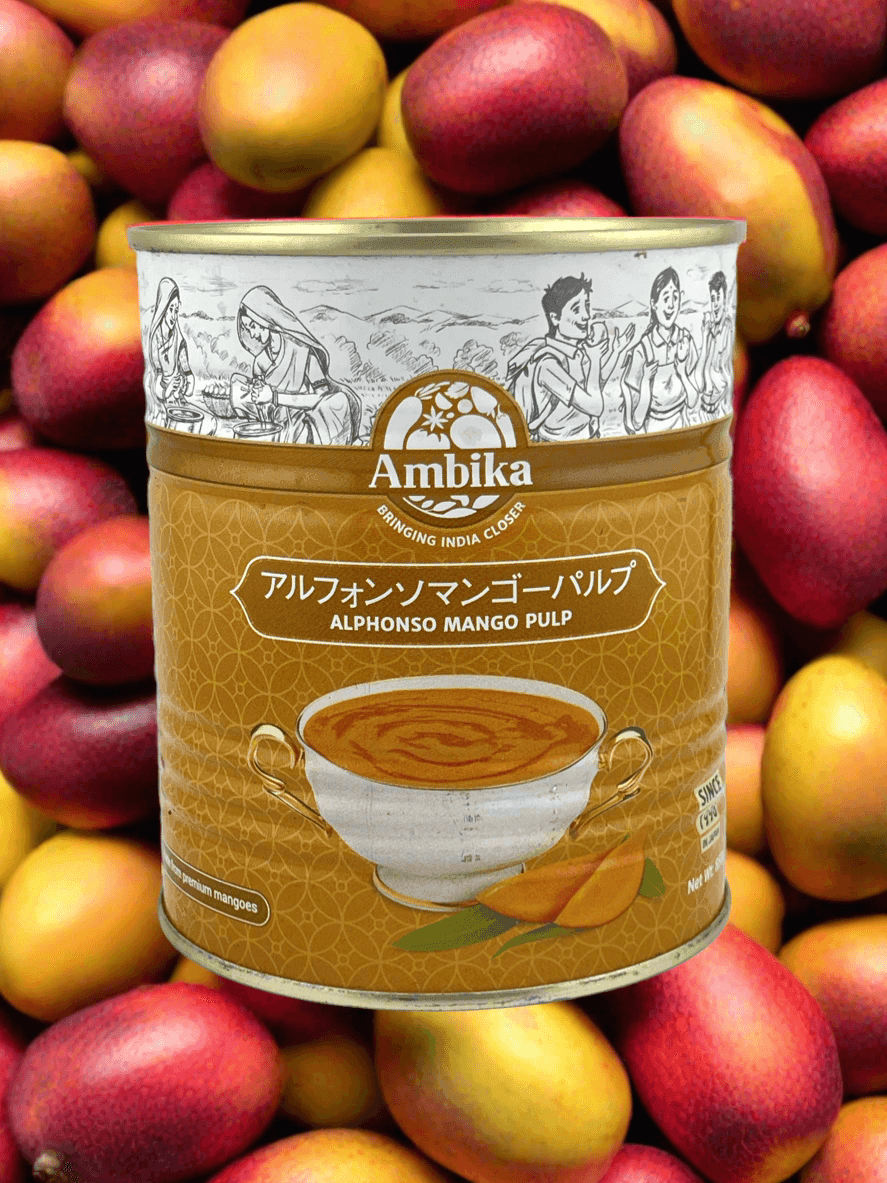 Can of Ambika Alphonso mango pulp with vintage Indian illustrations on label, surrounded by fresh mangoes