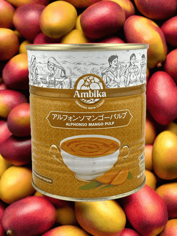 Can of Ambika Alphonso mango pulp with vintage Indian illustrations on label, surrounded by fresh mangoes