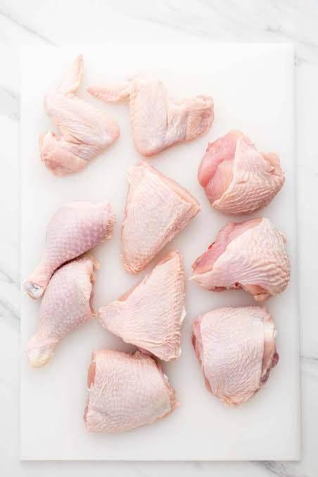 Raw assorted chicken parts including wings, drumsticks, and thighs on a white cutting board