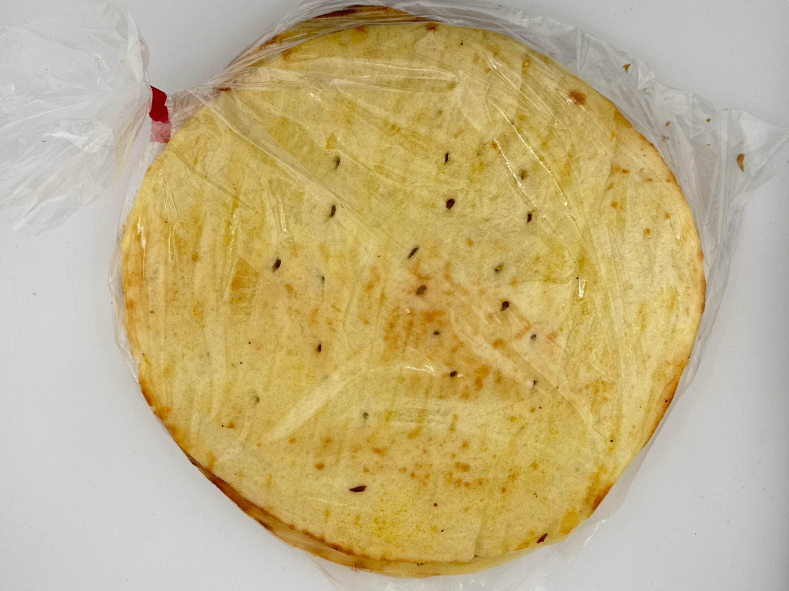 Packaged round flatbread with visible seasoning inside clear plastic wrap on white surface