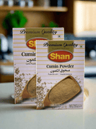 Two boxes of Shan Cumin Powder with wooden spoon and cumin seeds, premium quality spice packaging