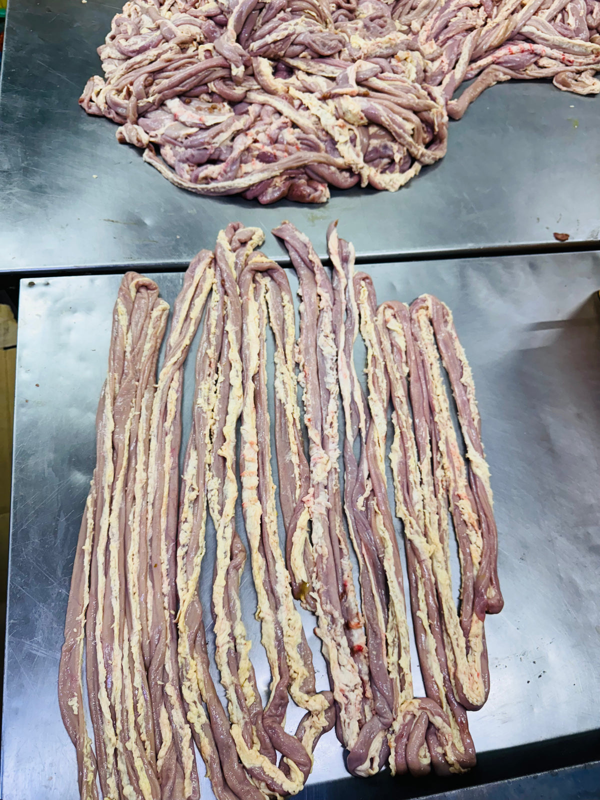 Raw animal intestines and tripe laid out on a stainless steel surface in a food processing area