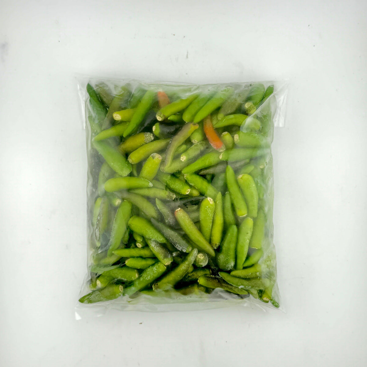 Vacuum-sealed plastic bag of fresh green chili peppers with a few red chilies on white background