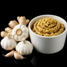 White bowl of ginger garlic paste with fresh garlic bulbs, garlic cloves, and ginger on black background