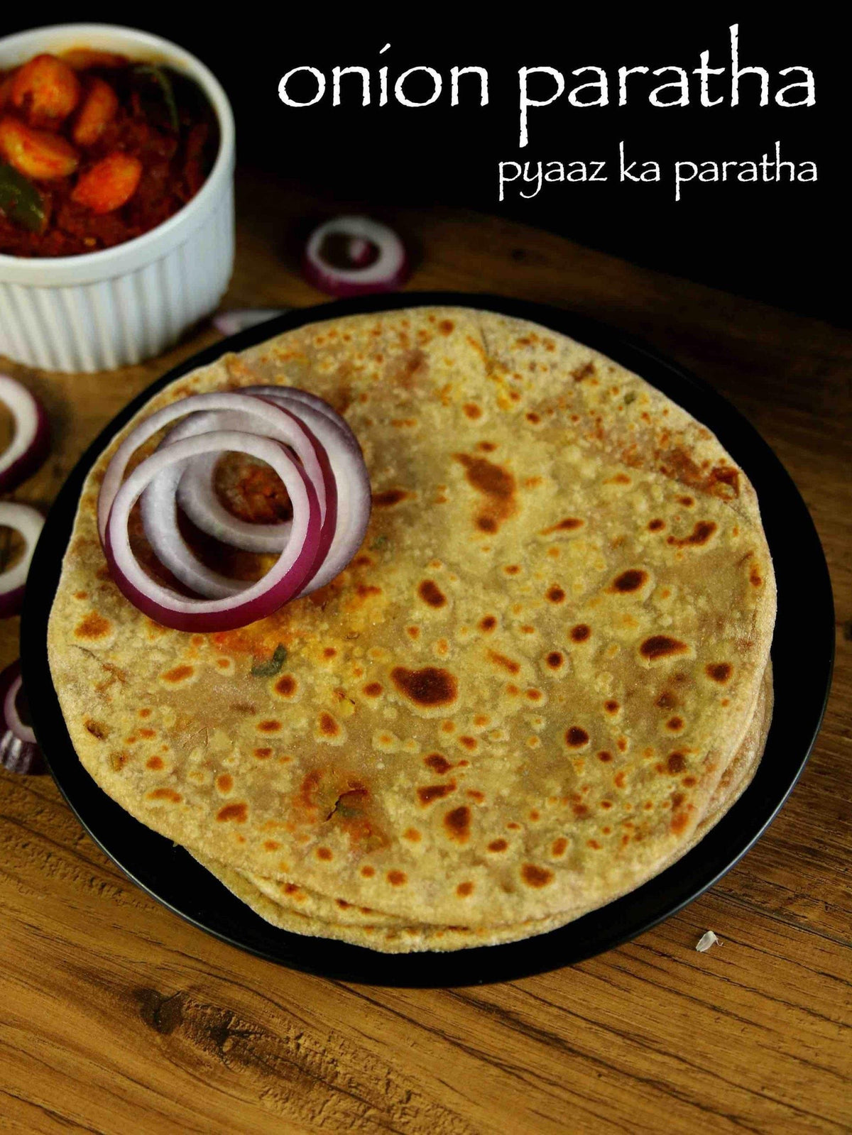 Onion paratha served on a black plate with raw onion rings and a side of spicy curry in a white bowl