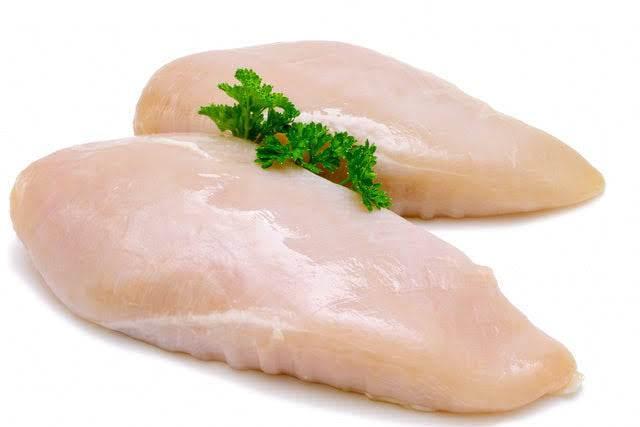 Two raw chicken breasts garnished with fresh parsley on a white background