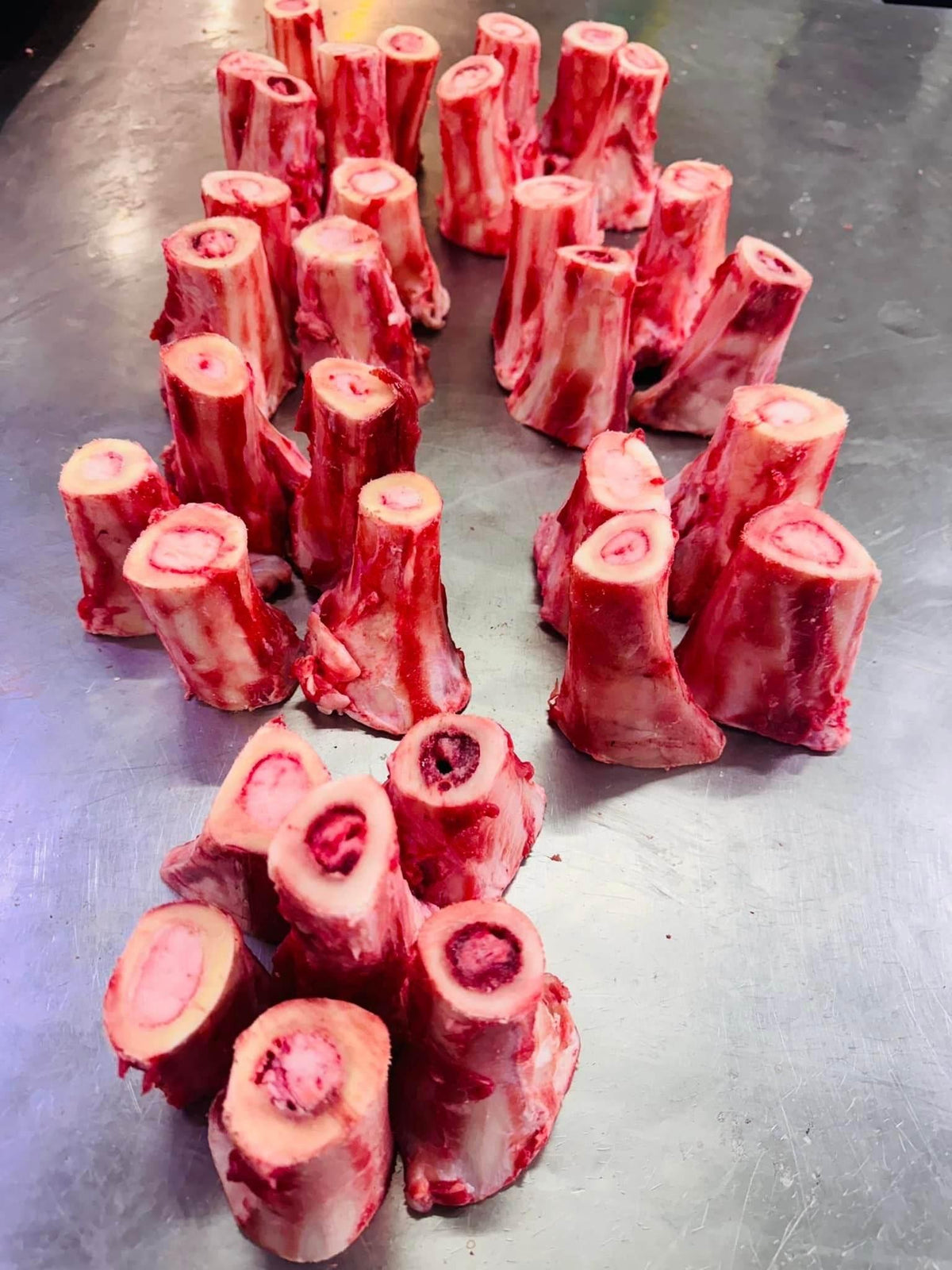Cut pieces of raw beef marrow bones arranged on a metal surface, ready for cooking or sale