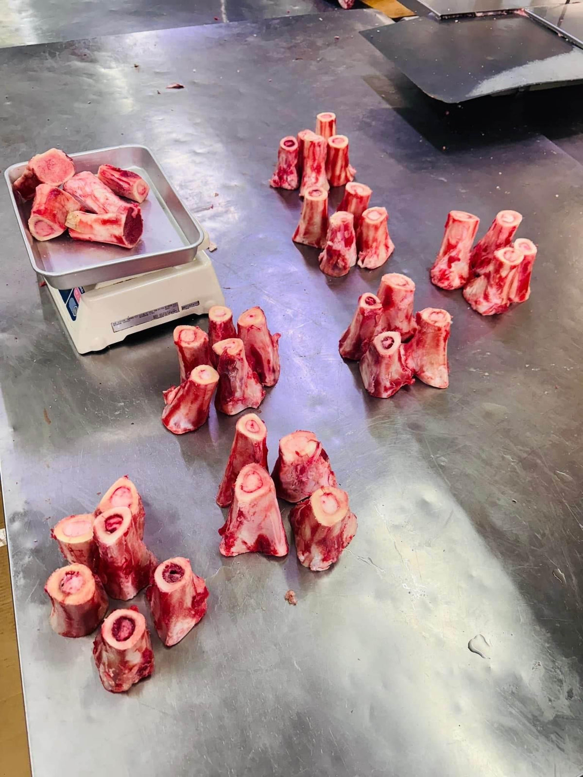 Raw beef marrow bones grouped on a stainless steel counter with a metal tray scale in a butcher shop