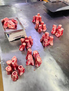 Raw beef marrow bones grouped on a stainless steel counter with a metal tray scale in a butcher shop