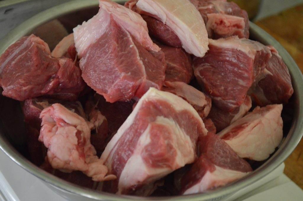 Raw beef meat chunks with fat in a metal bowl, ready for cooking or stew