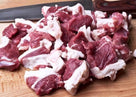 Raw fresh beef chunks with fat on wooden cutting board beside kitchen knife