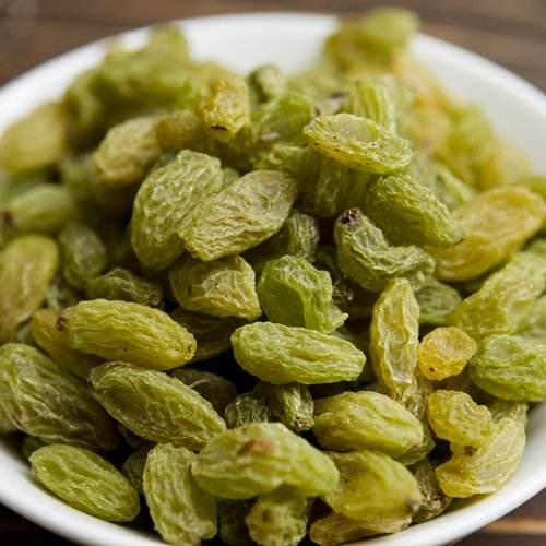 Close-up of green raisins piled in a white bowl on a wooden surface