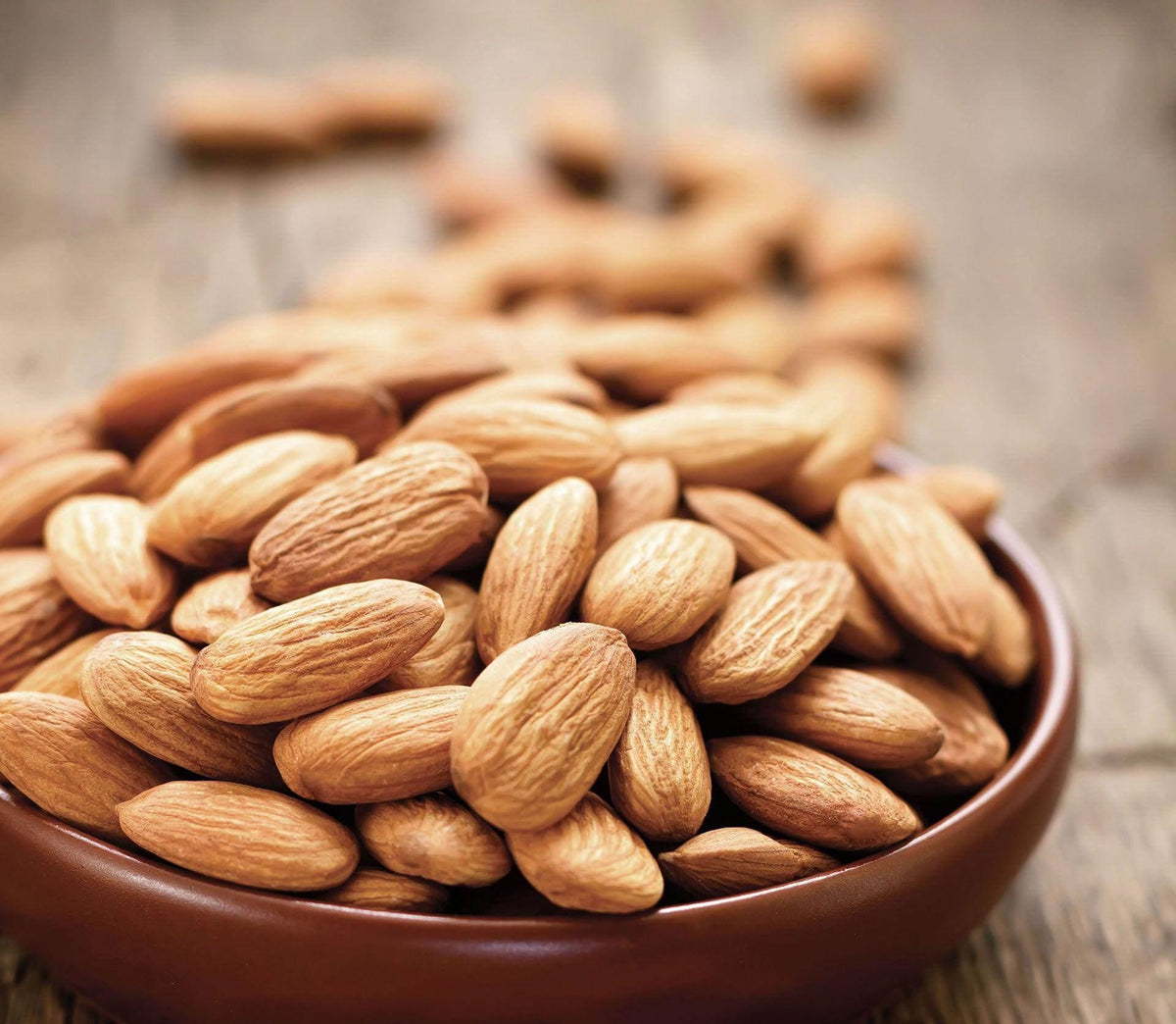 Close-up of whole raw almonds in a brown bowl on a wooden surface