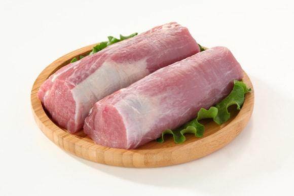 Two raw pork tenderloins on wooden plate with green lettuce on white background