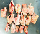 Raw frozen goat tails on metal surface, fresh meat cuts with visible fat and bone