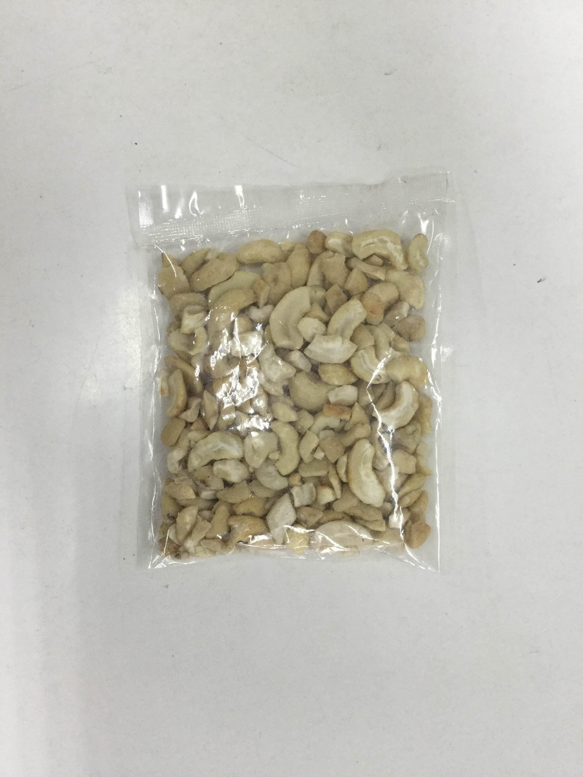 Clear plastic bag filled with mixed broken cashew nuts on a white surface