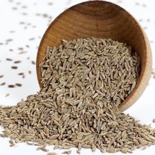 Close-up of wooden bowl spilling dried cumin seeds on white surface