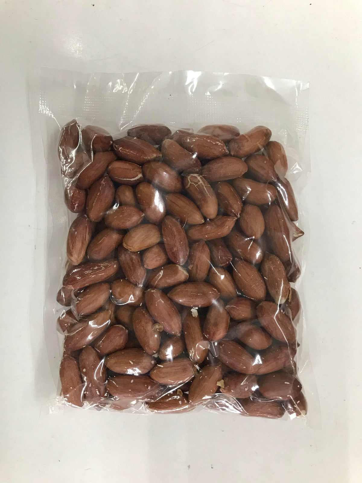 Clear plastic bag filled with raw unshelled peanuts on a white surface