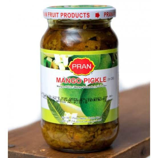 Jar of Pran brand mango pickle in oil with green mangoes on label on wooden surface