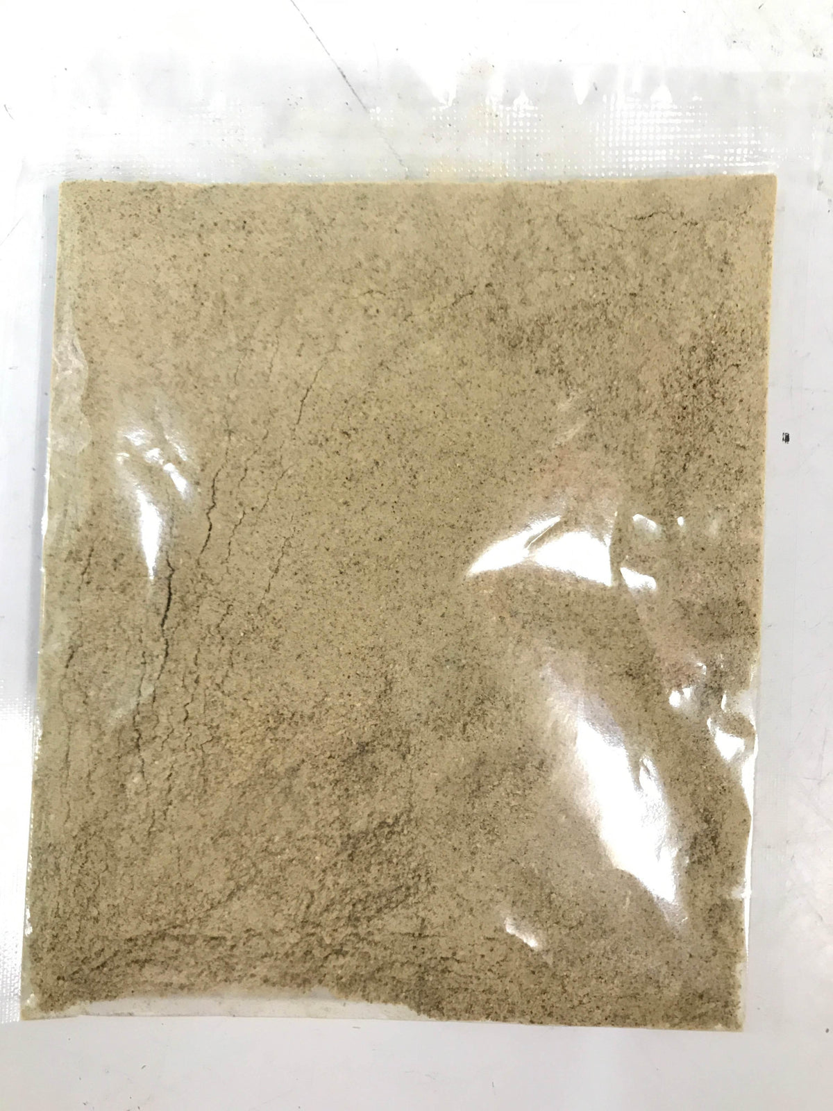 Clear plastic packet containing fine beige powder on white surface