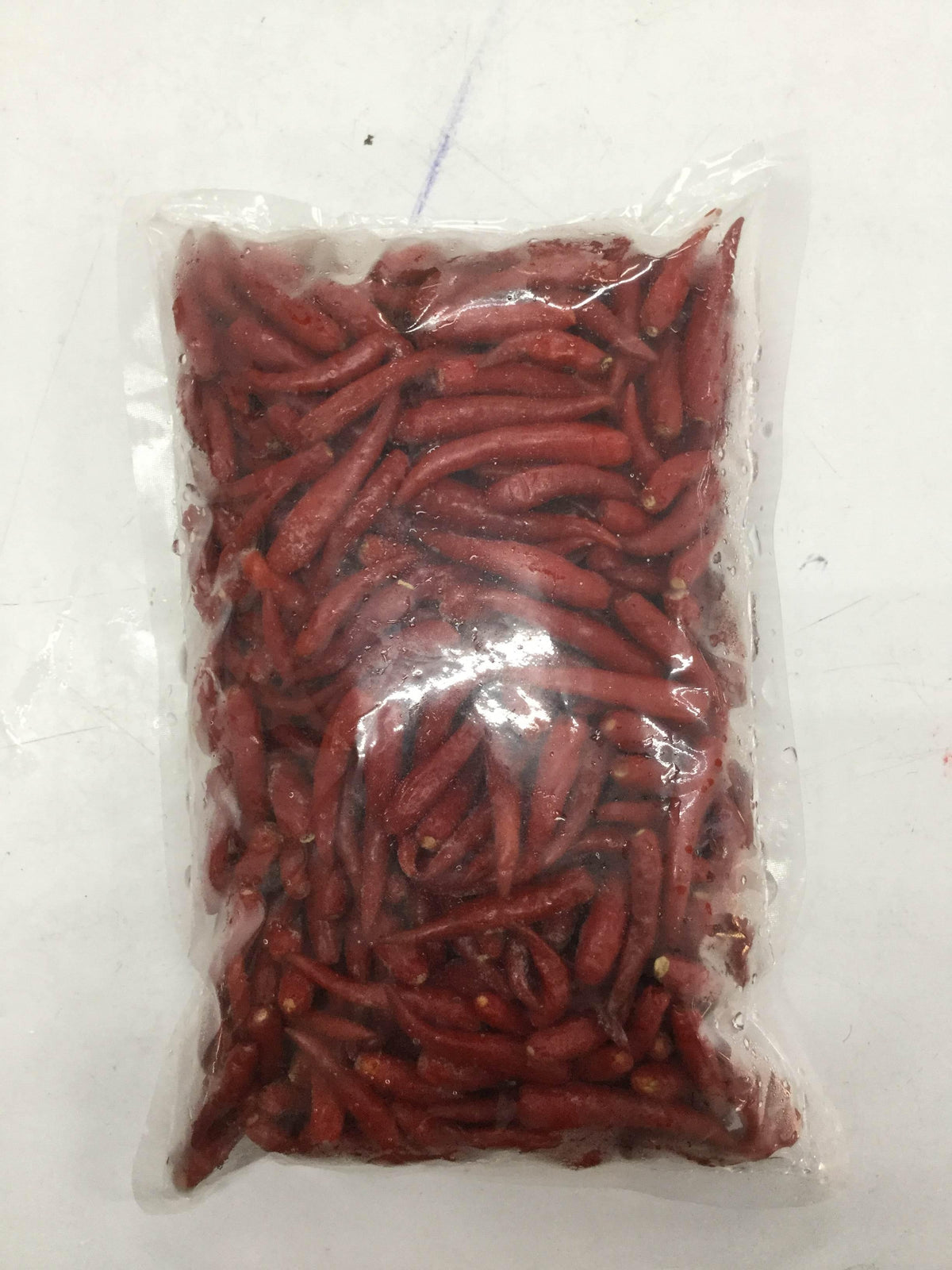 Vacuum-sealed clear plastic bag containing small red chili peppers on a white surface