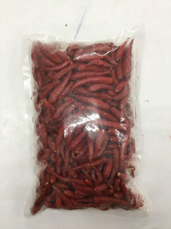 Vacuum-sealed clear plastic bag containing small red chili peppers on a white surface