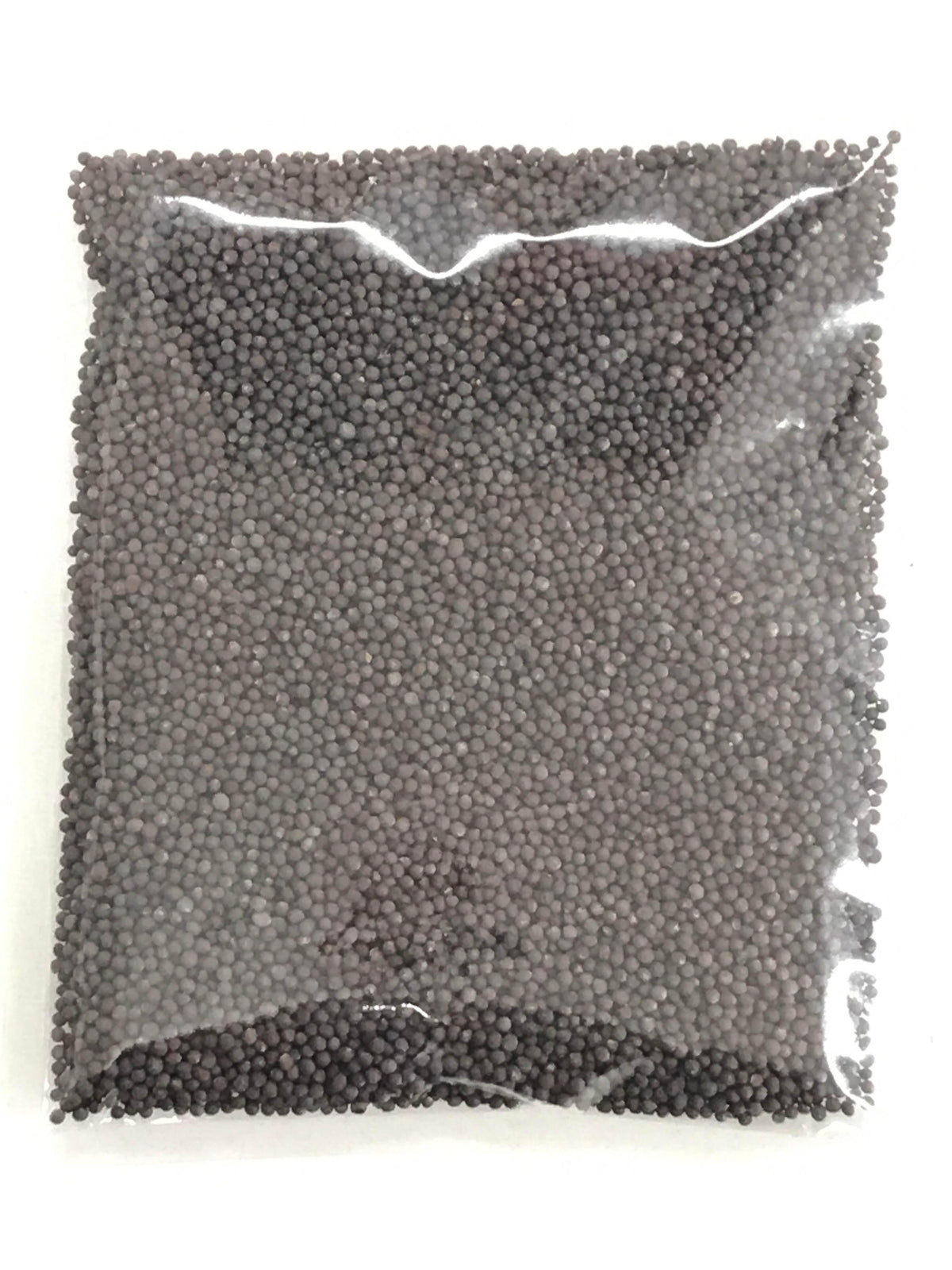 Clear plastic bag filled with tiny round black beads or seeds on a white background