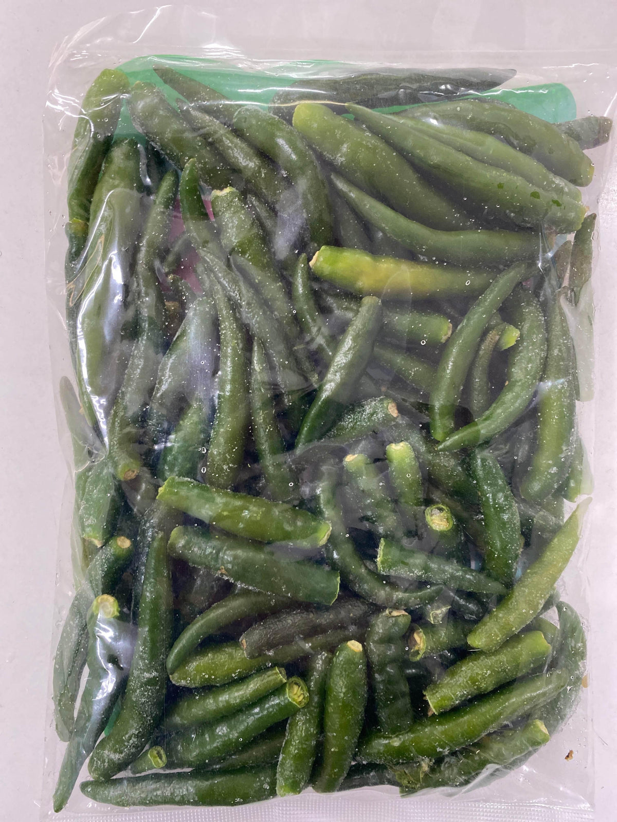 Clear plastic bag filled with frozen green chili peppers on a plain surface