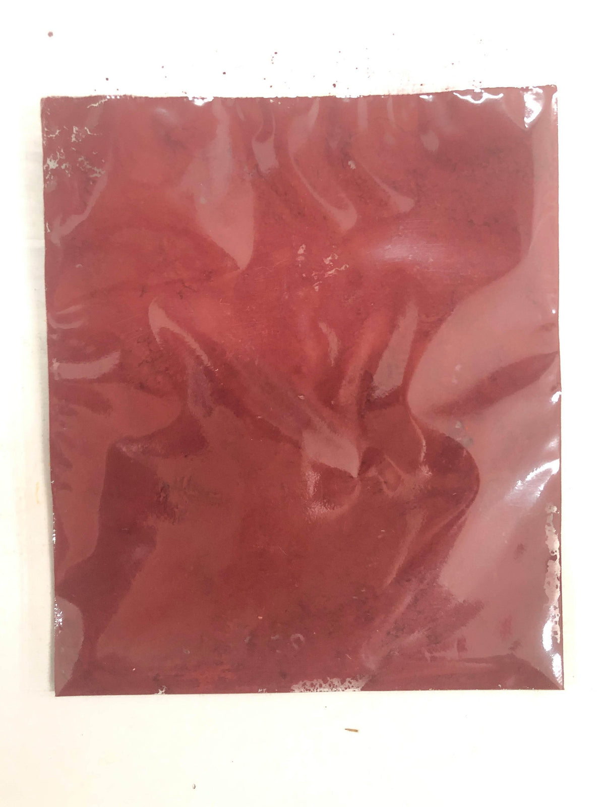 Vacuum-sealed transparent plastic bag containing red powdered pigment on a white surface