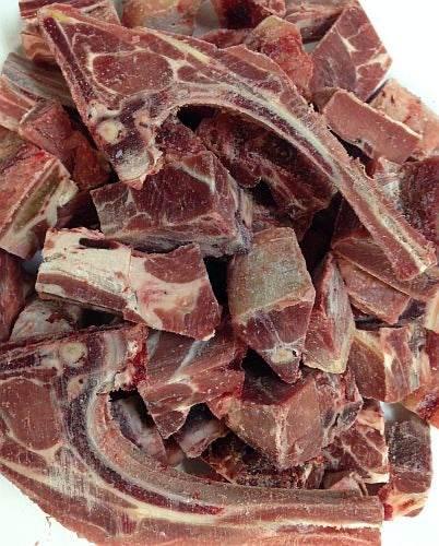 pile of raw frozen goat meat pieces with bone on a white background