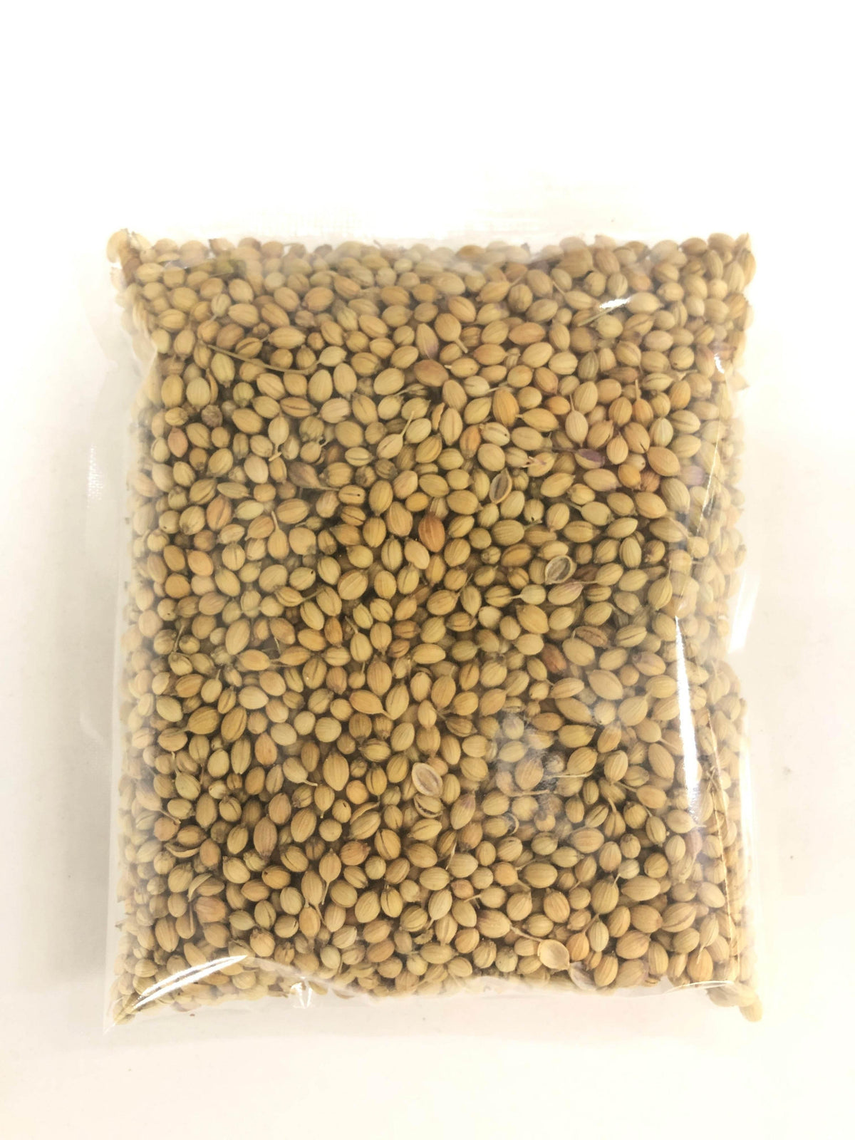 Clear plastic bag filled with light brown coriander seeds on white surface