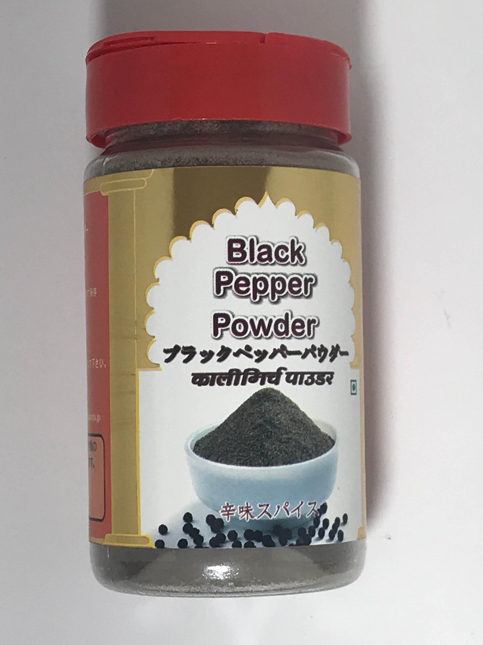 Glass jar of black pepper powder with red lid and label showing powder in white bowl and black peppercorns