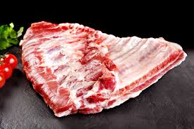 Raw pork ribs on black slate with cherry tomatoes and greens