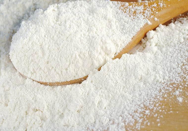 Close-up of white wheat flour maida on a wooden spoon and surface
